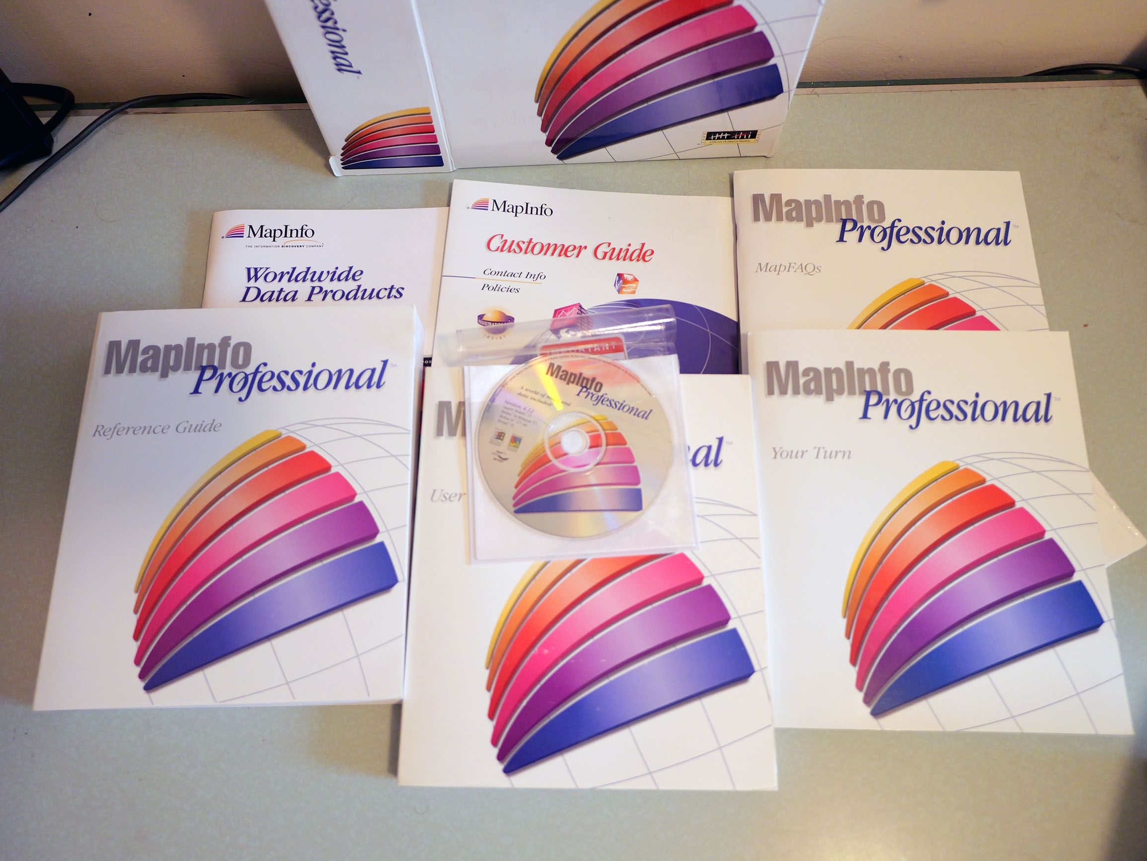The contents of the MapInfo box, which includes a User Manual, something called MapFAQs, a Reference Guide, and of course the product CD-ROM. All of these items have the sphere logo guy on them.