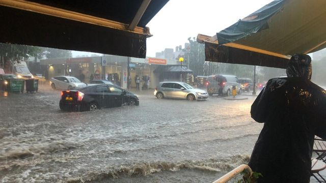A flooded street with cars and umbrellas Description automatically generated