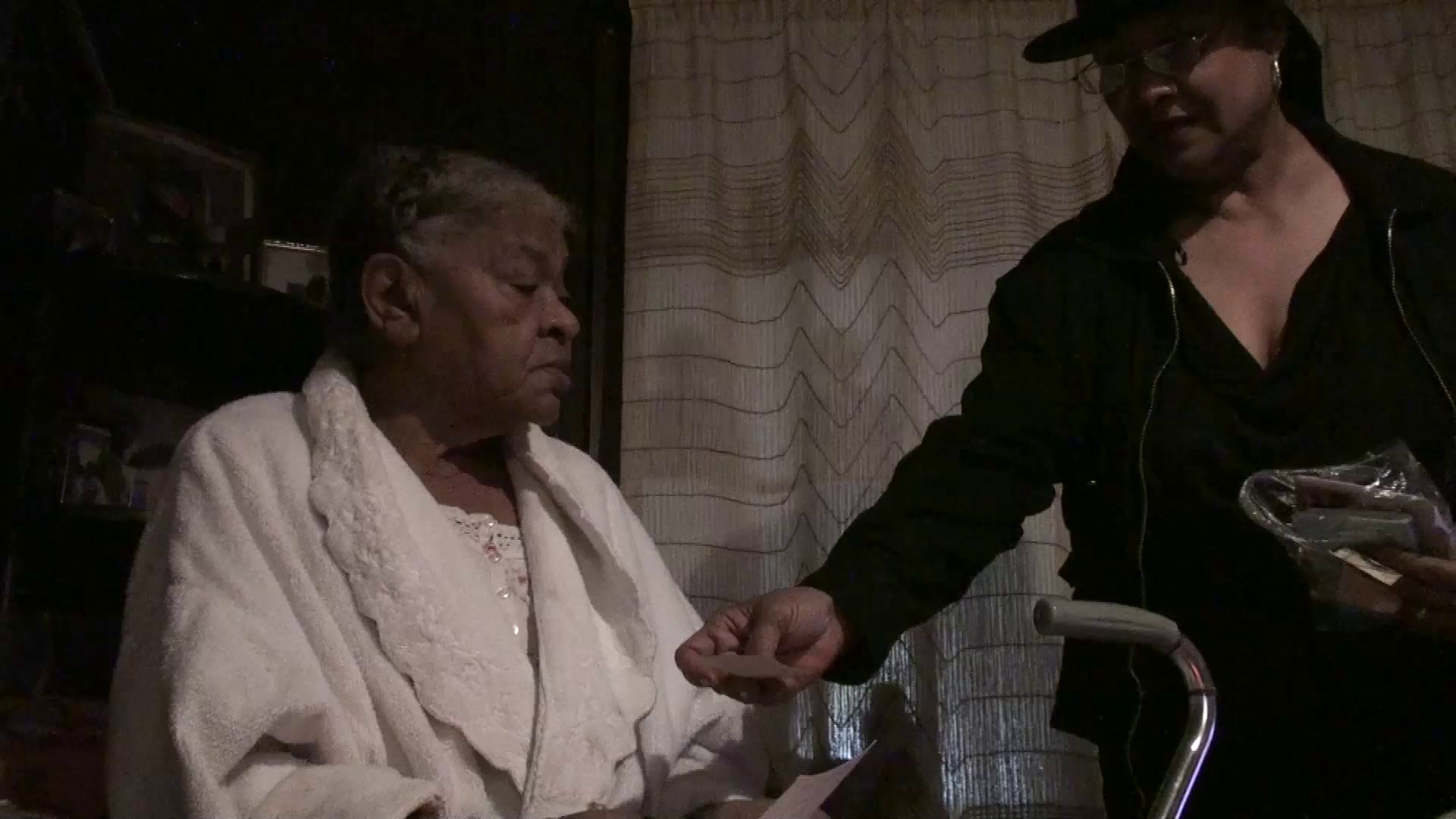 Emma Sims (left) seated in her home in Centreville, Miss. Catherine Walker Jones holds out a wallet sized photo of her father, as she asks Sims what she knows about the murder. Photo by Ben Greenberg