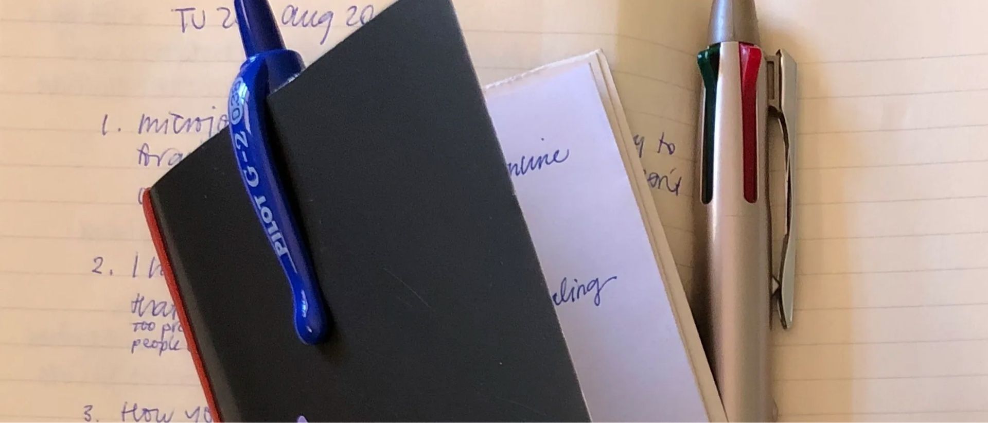 A small notebook sits on the open pages of a larger book, both contain handwritten notes