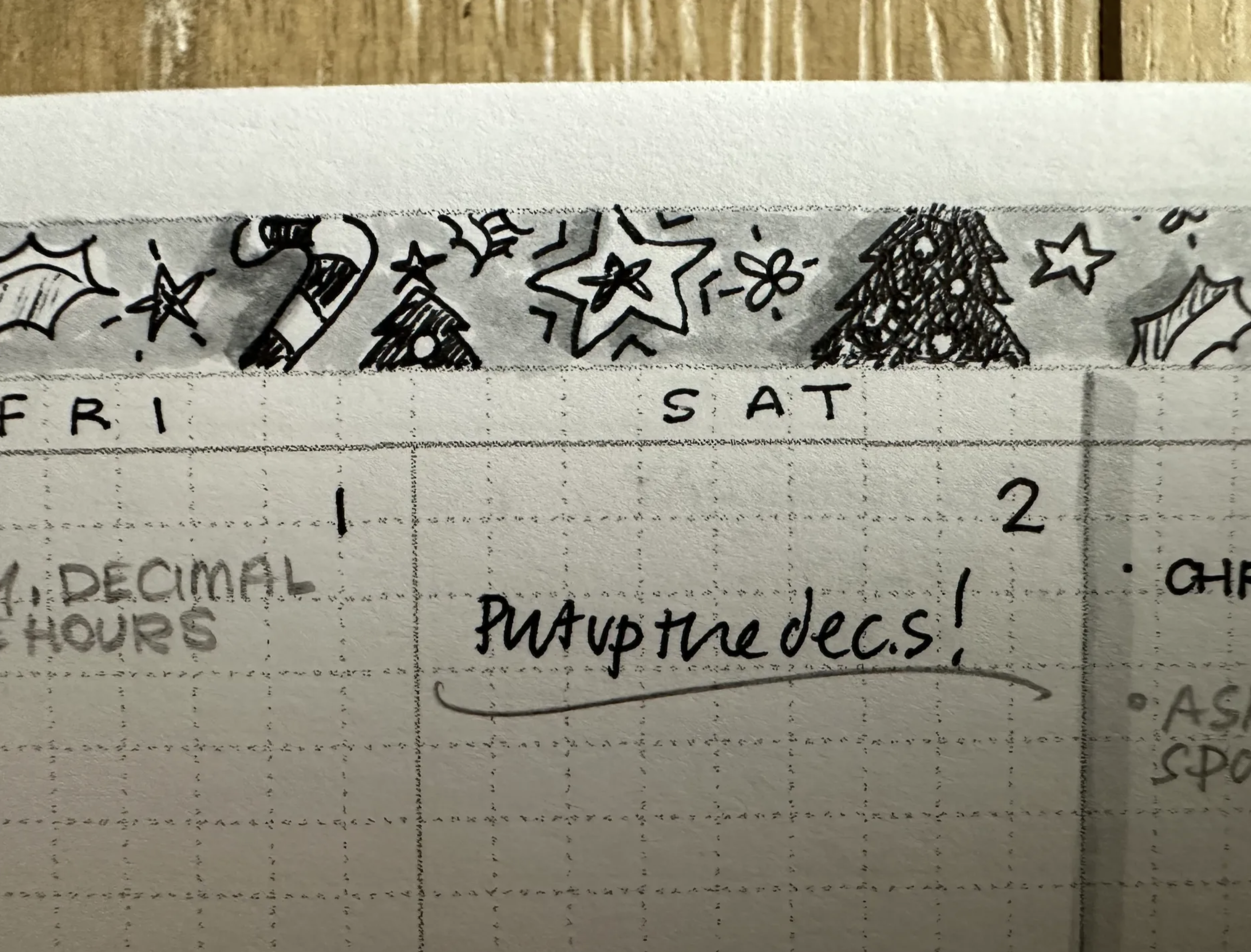 closeup of a white page with a partial view of 3 days of a month on grid paper. christmas decoration sketches in black, white and grey ink