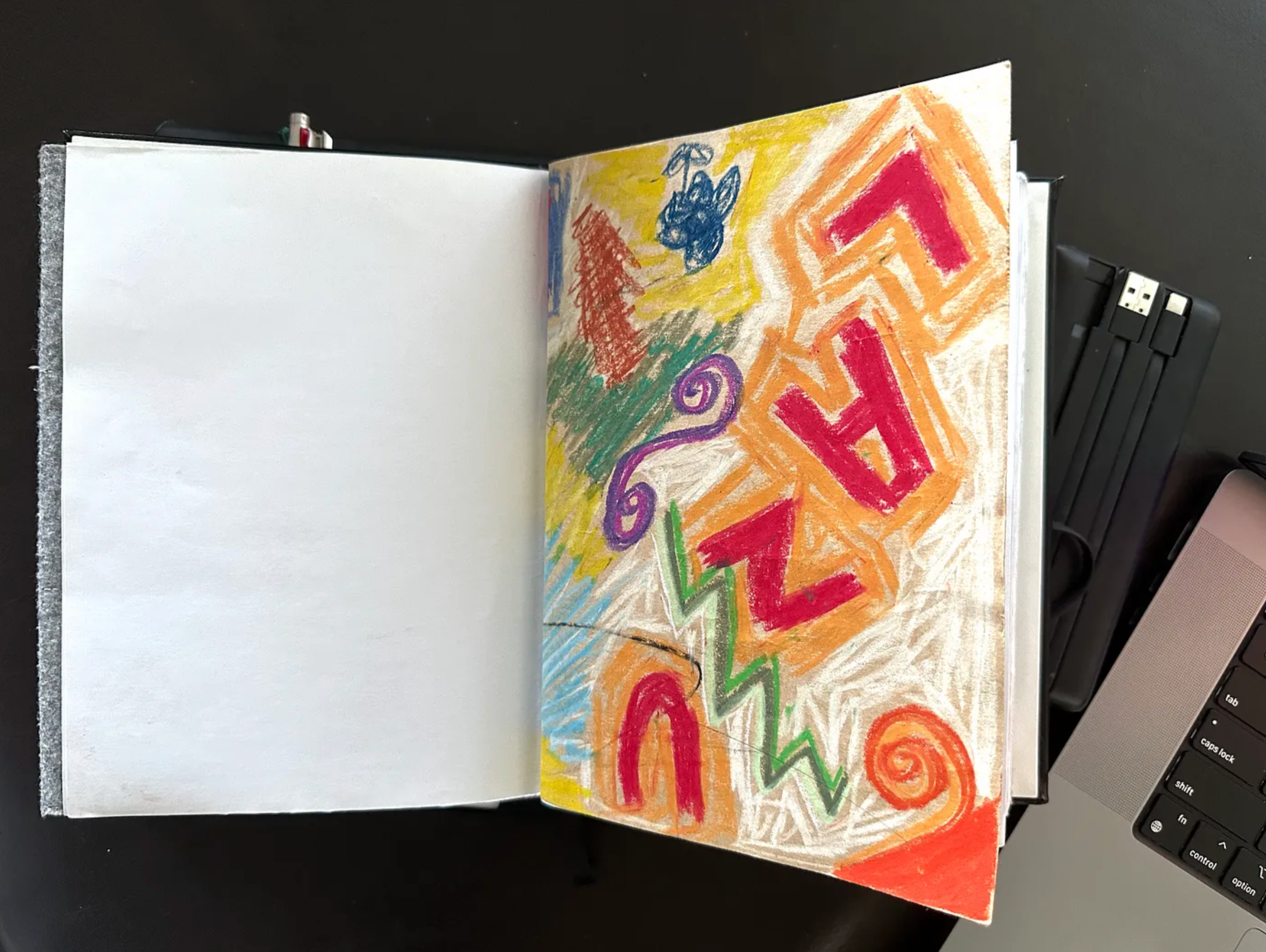 An open notebook on a dark background, with an adult’s crayon drawing on brown paper on the right hand page.