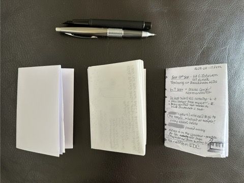 Three A6 sized booklets, folded from larger sheets of paper. There is a mechanical pencil and a black fountain pen nearby.