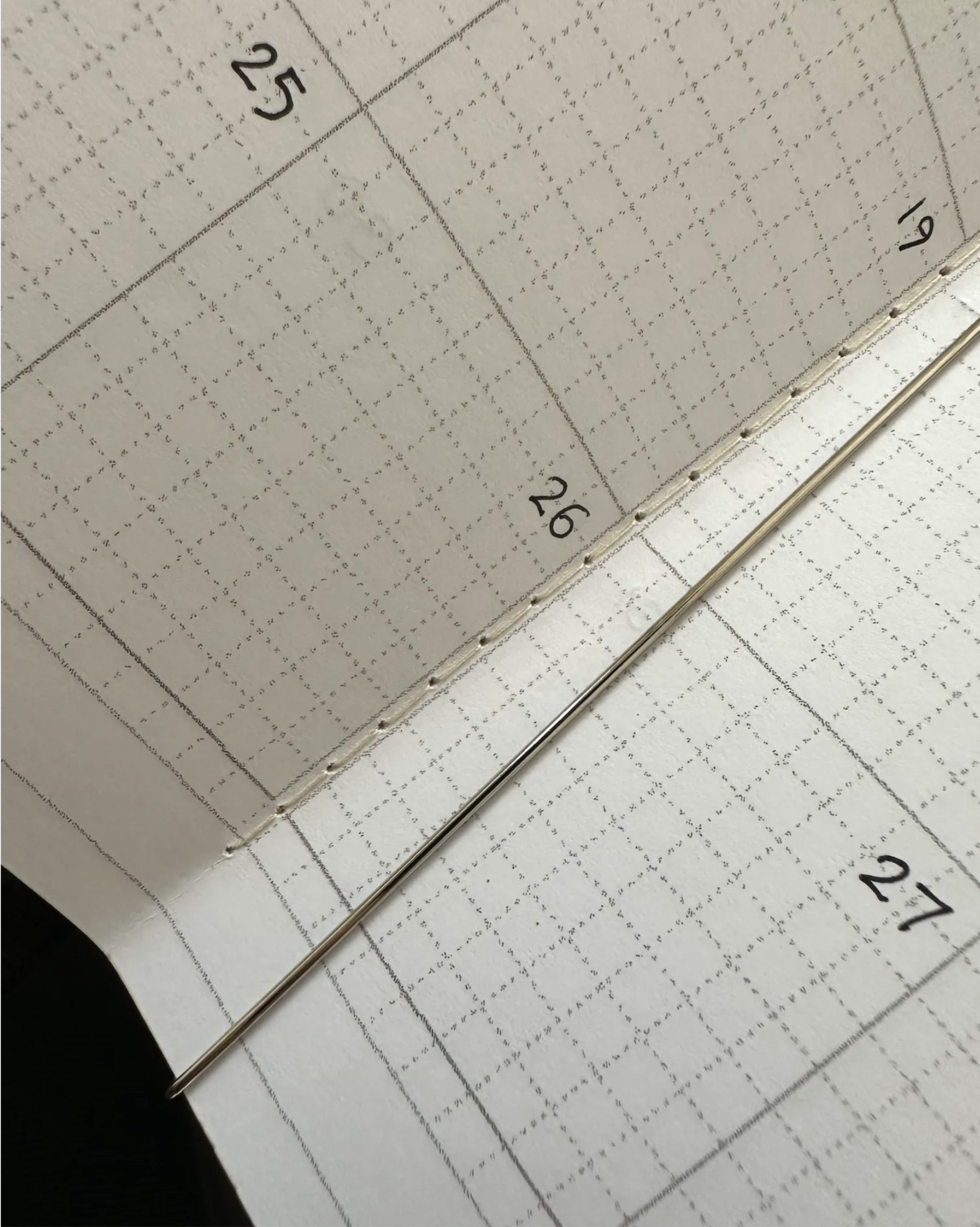 stitched pages sit under a metal bar; there’s a grid showing a partial view of several days of a month