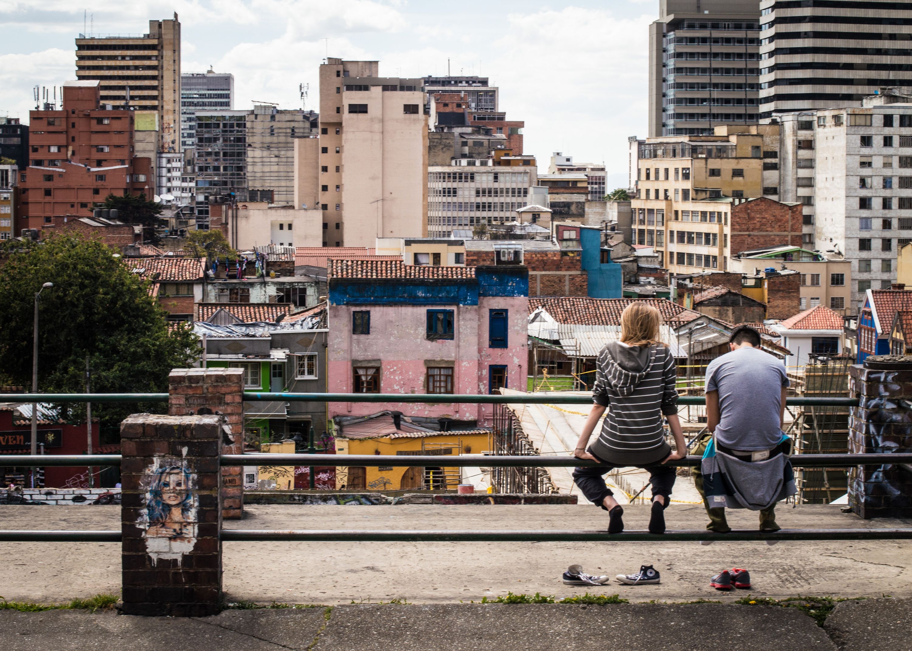 photo of two people sitting on railing overlooking dense city landscape of high-rise buildings