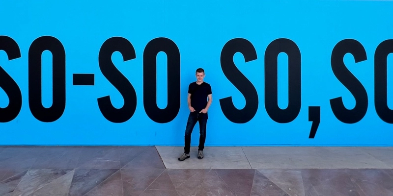 Ken standing in front of a blue wall between the letters so so