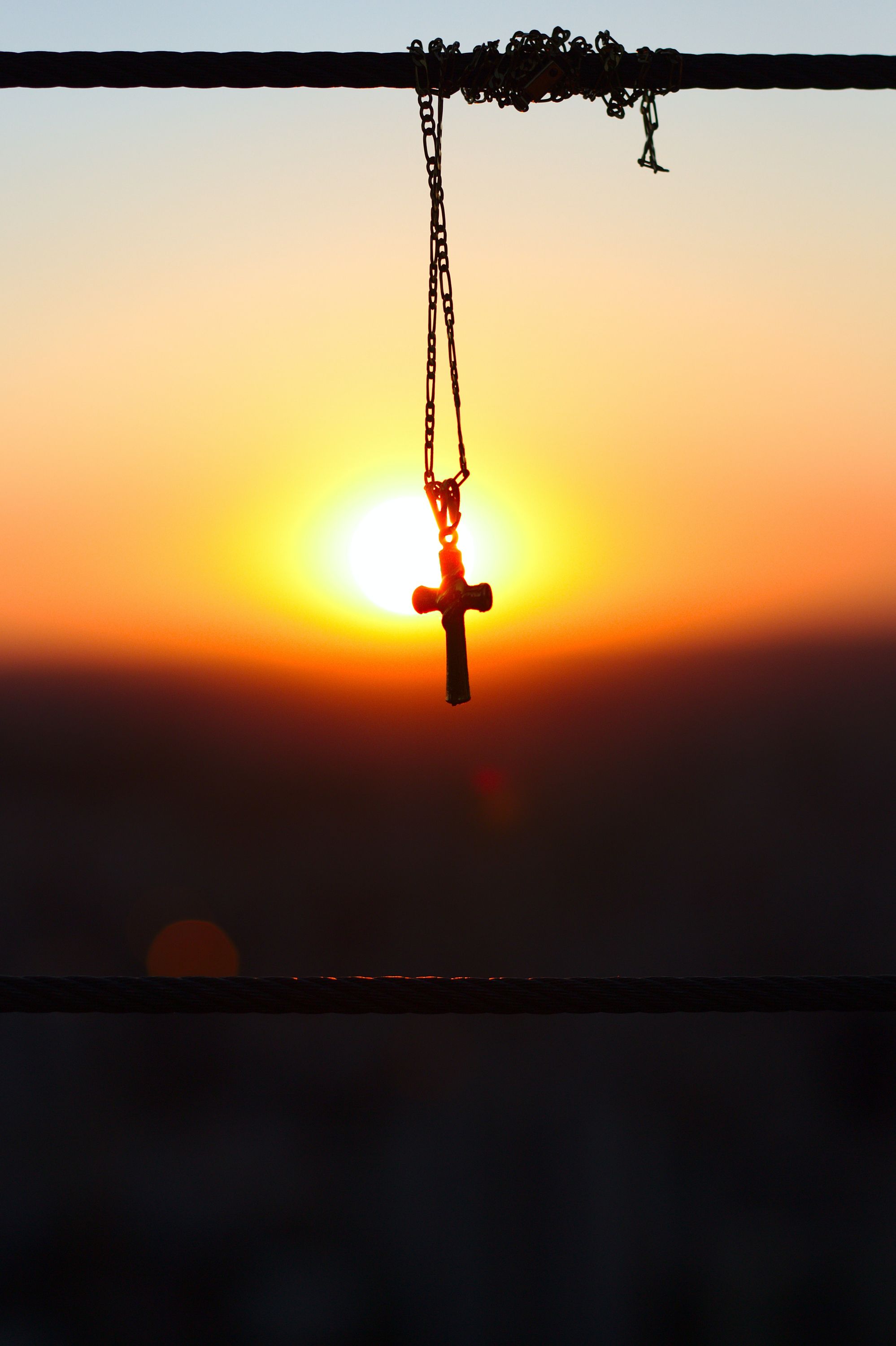 Photo of a sunset with a cross necklace in the middle.