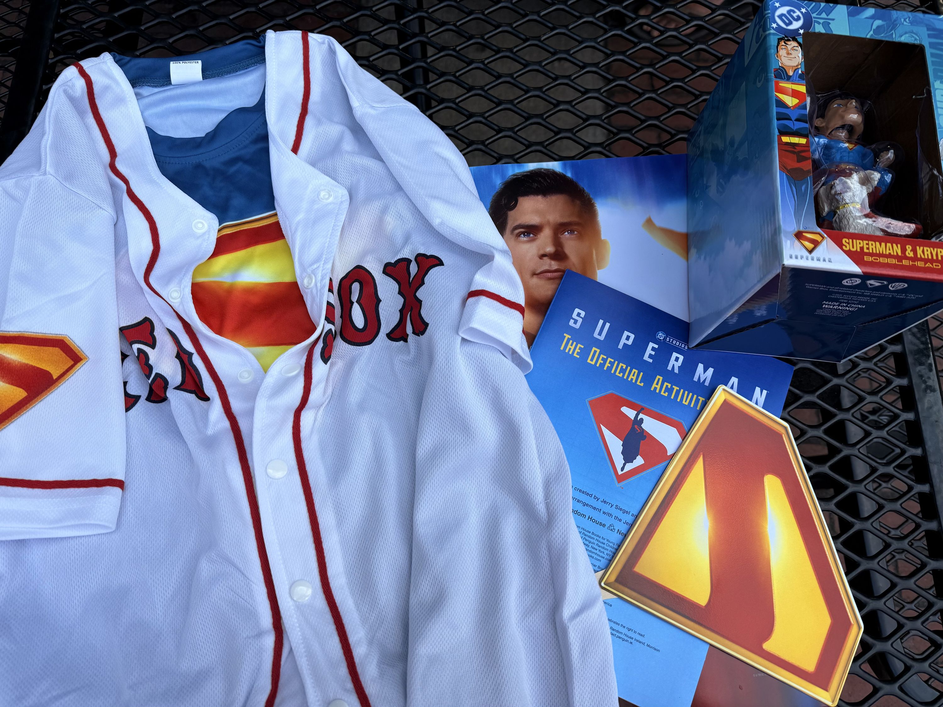 A Superman Red Sox Jersey, a Superman and Krypto baseball bobblehead, a Superman poster, a Superman hand fan, and a Superman activity book.