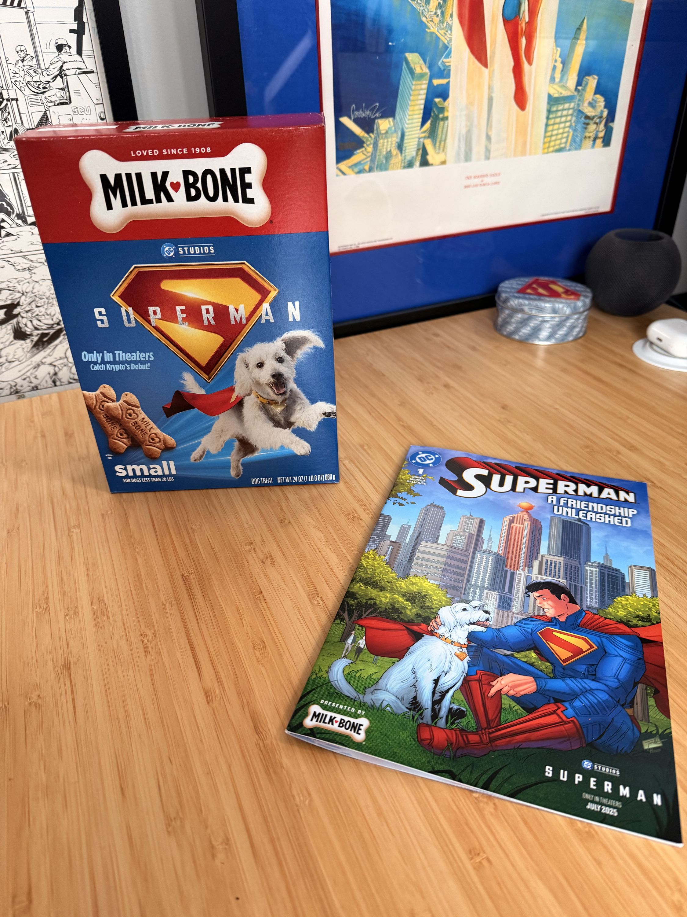 A box of milk bone dog treats with the Superman movie logo and Krypto the superdog flying. Next to that is a comic book Superman a friendship unleashed. Superman is sitting with krypto on the cover.