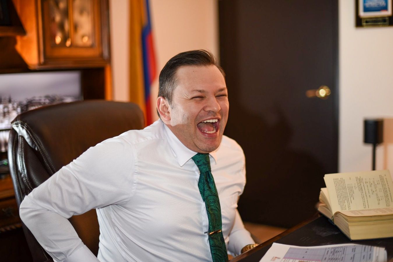 A person in a white shirt and green tie laughing Description automatically generated