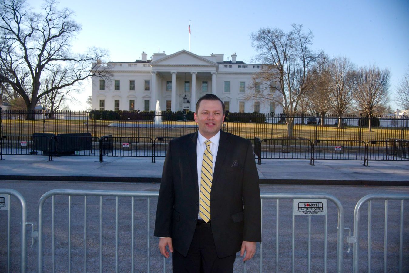 A person in a suit standing in front of a white house Description automatically generated