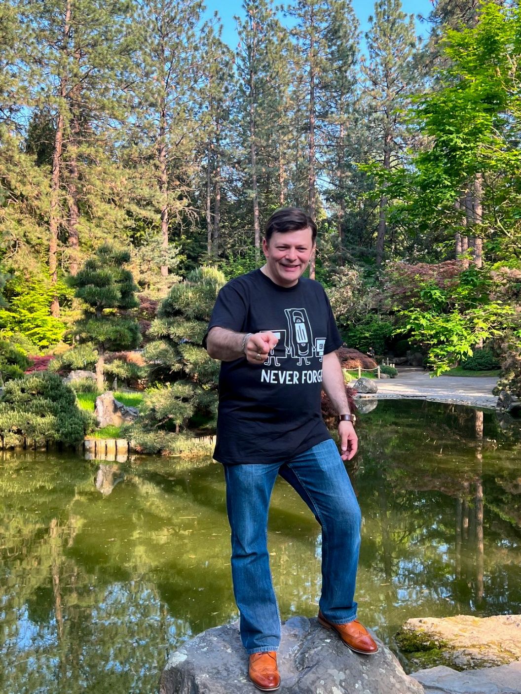 A person standing on a rock in front of a pond Description automatically generated