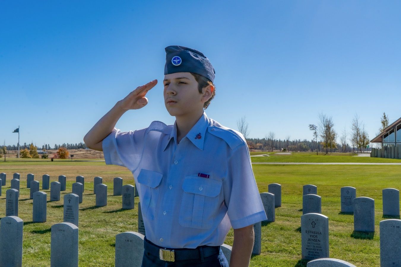 A child saluting in a cemetery Description automatically generated