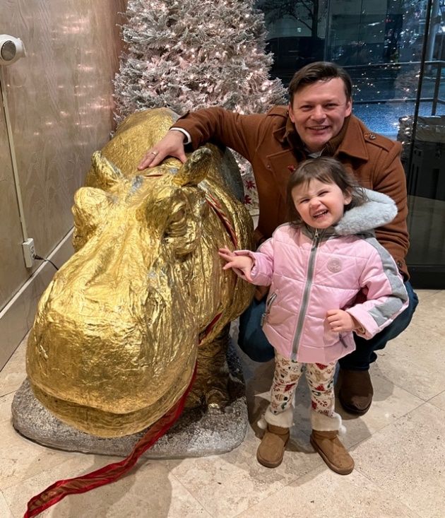 A person and a child posing with a statue of a hippo Description automatically generated