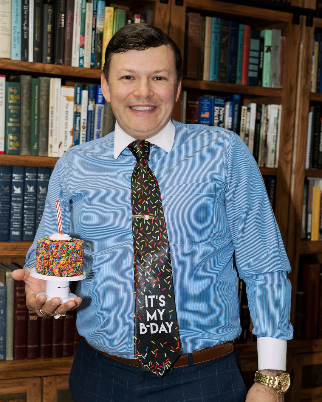 A person wearing a tie and tie holding a birthday cake Description automatically generated