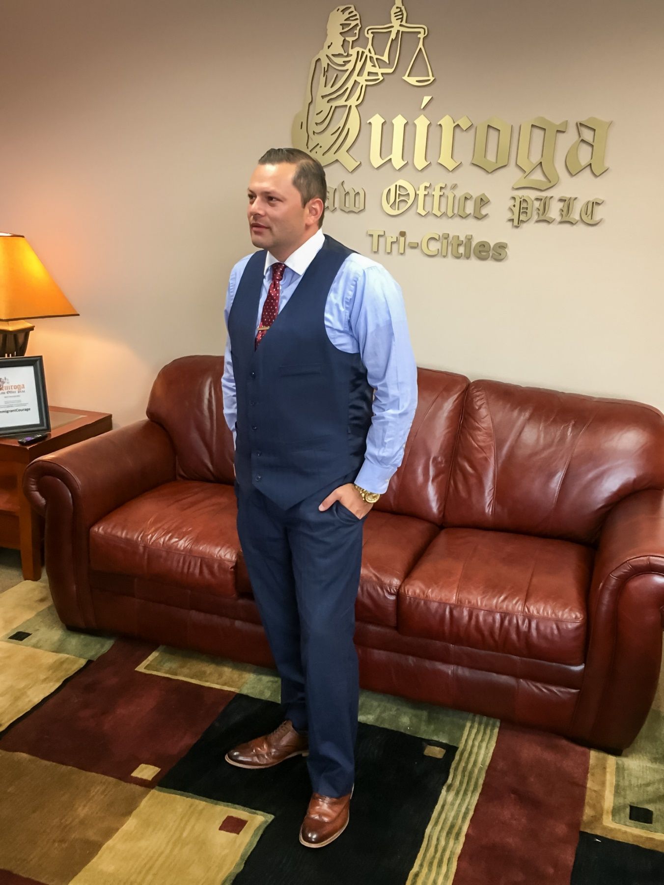 A person in a suit standing in front of a couch Description automatically generated