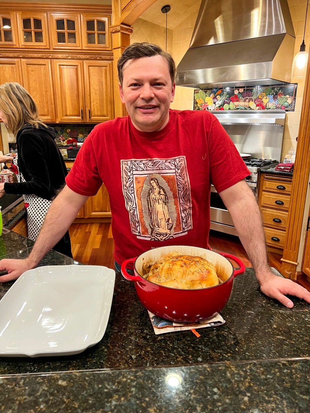 A person standing in a kitchen with a red pot of food Description automatically generated