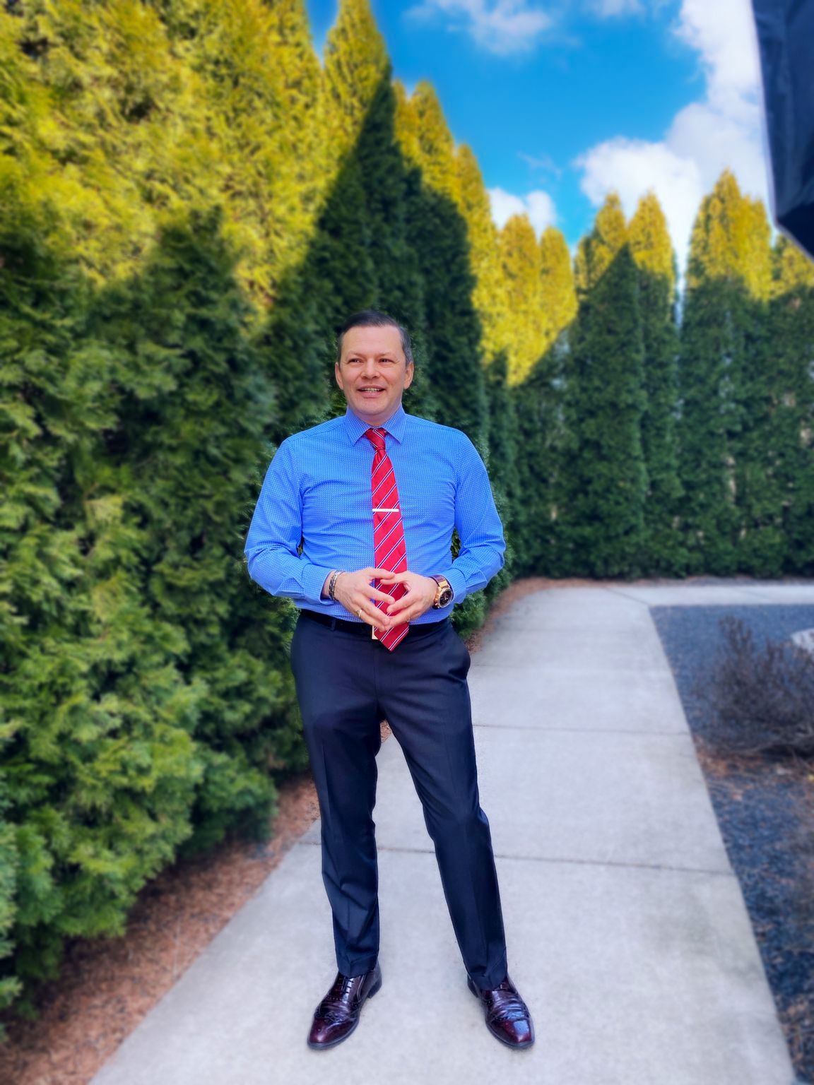 A person in a blue shirt and red tie standing on a sidewalk Description automatically generated