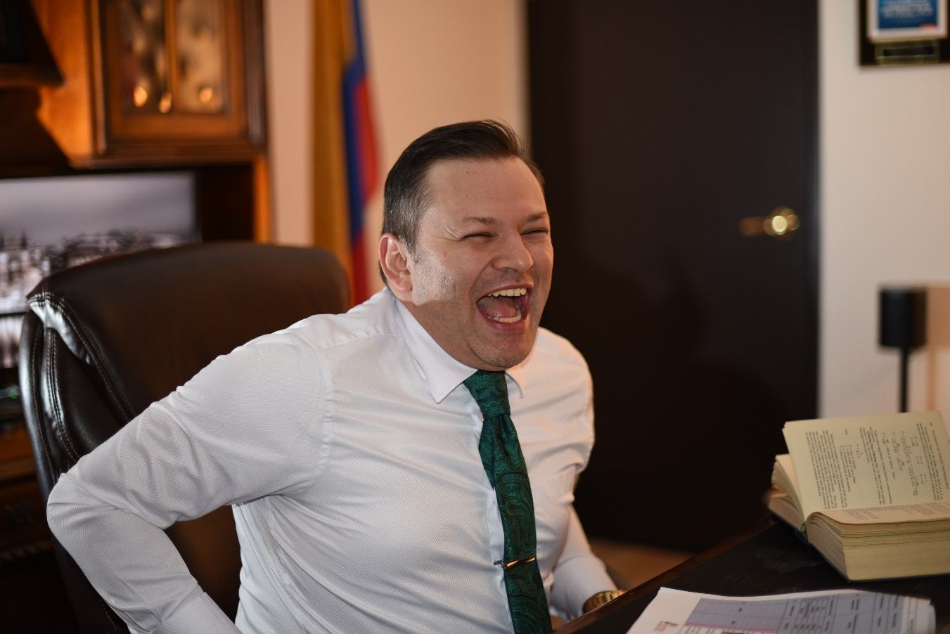 A person in a white shirt and green tie laughing Description automatically generated