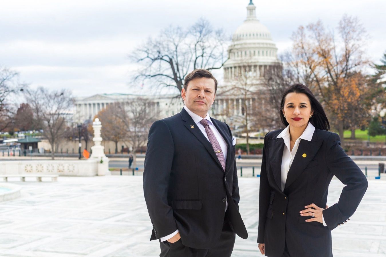 A person and person in suits standing in front of a building Description automatically generated