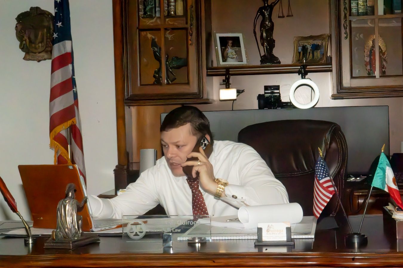 A person in a white shirt and tie sitting at a desk talking on the phone Description automatically generated