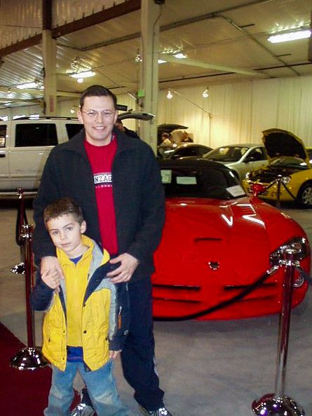 A person and child standing in front of a red car Description automatically generated