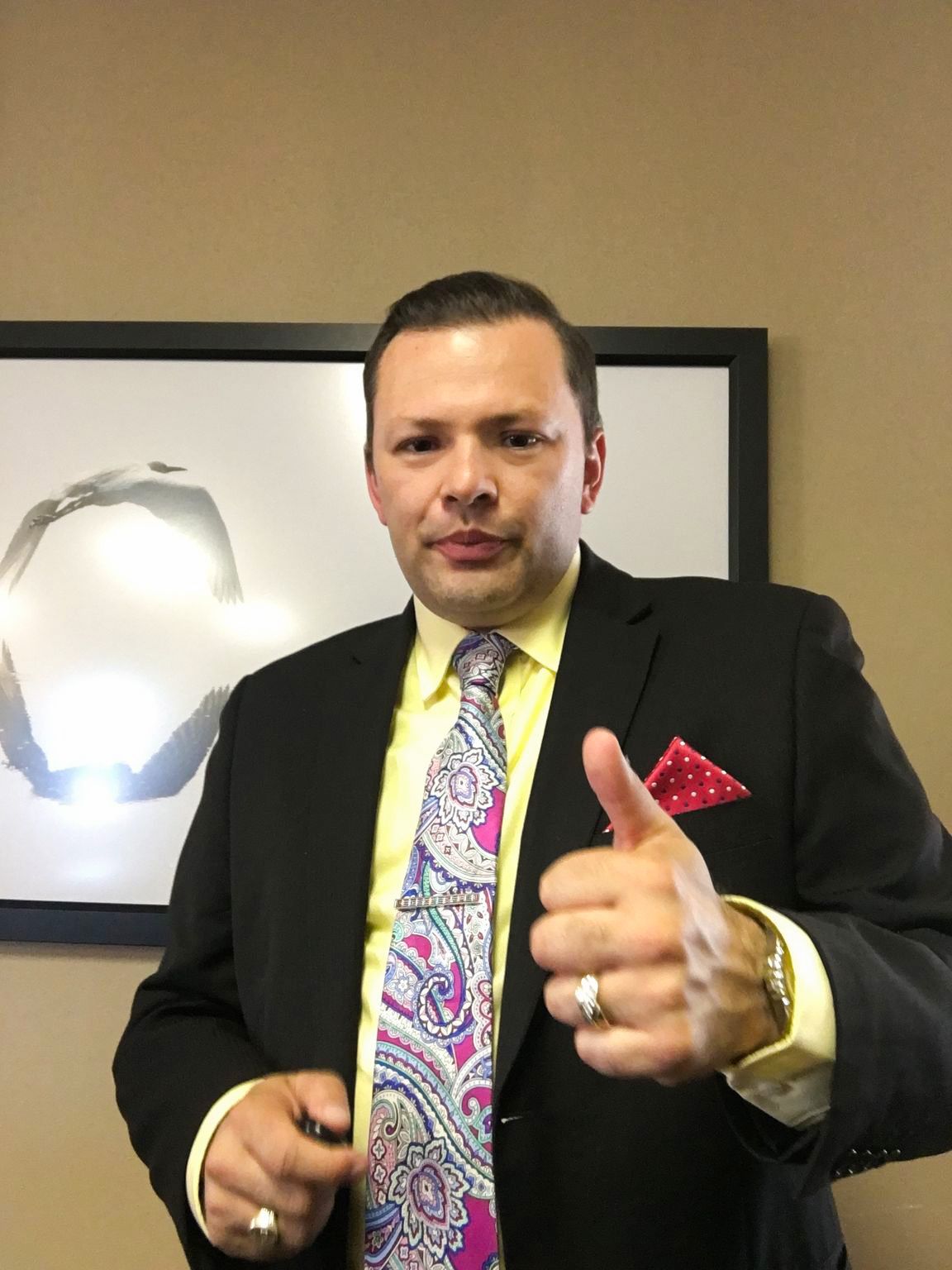 A person in a suit giving a thumbs up Description automatically generated