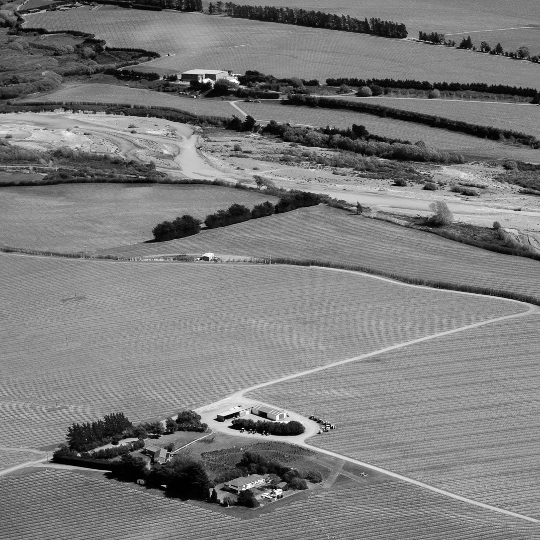 Aerial shot of farmland in New Zealand. A farmhouse is in the bottom, with zigzagging roads and fences moving up through the frame.