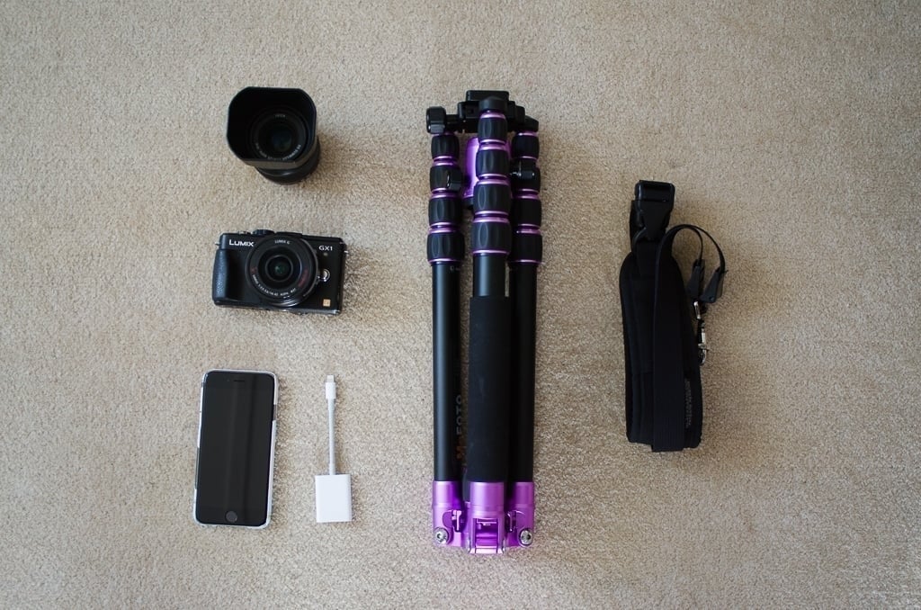 A camera, a spare lens, an iPhone, a tripod, and a carry strap