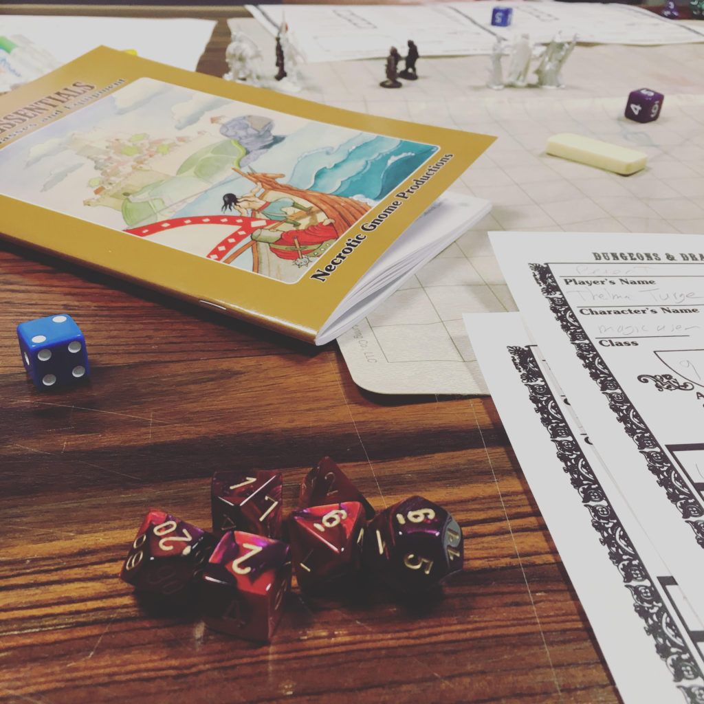 Tabletop with dice, miniatures, rulebook and character sheets.