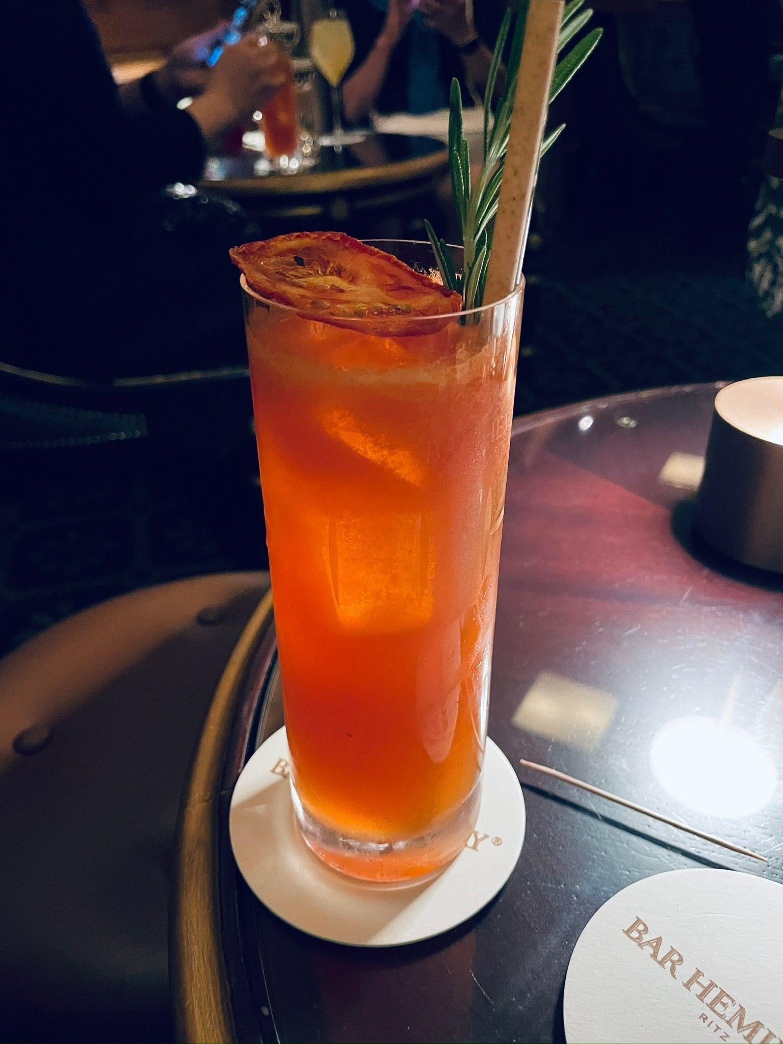 A glass of orange liquid with a straw and a rosemary leaf AI-generated content may be incorrect.