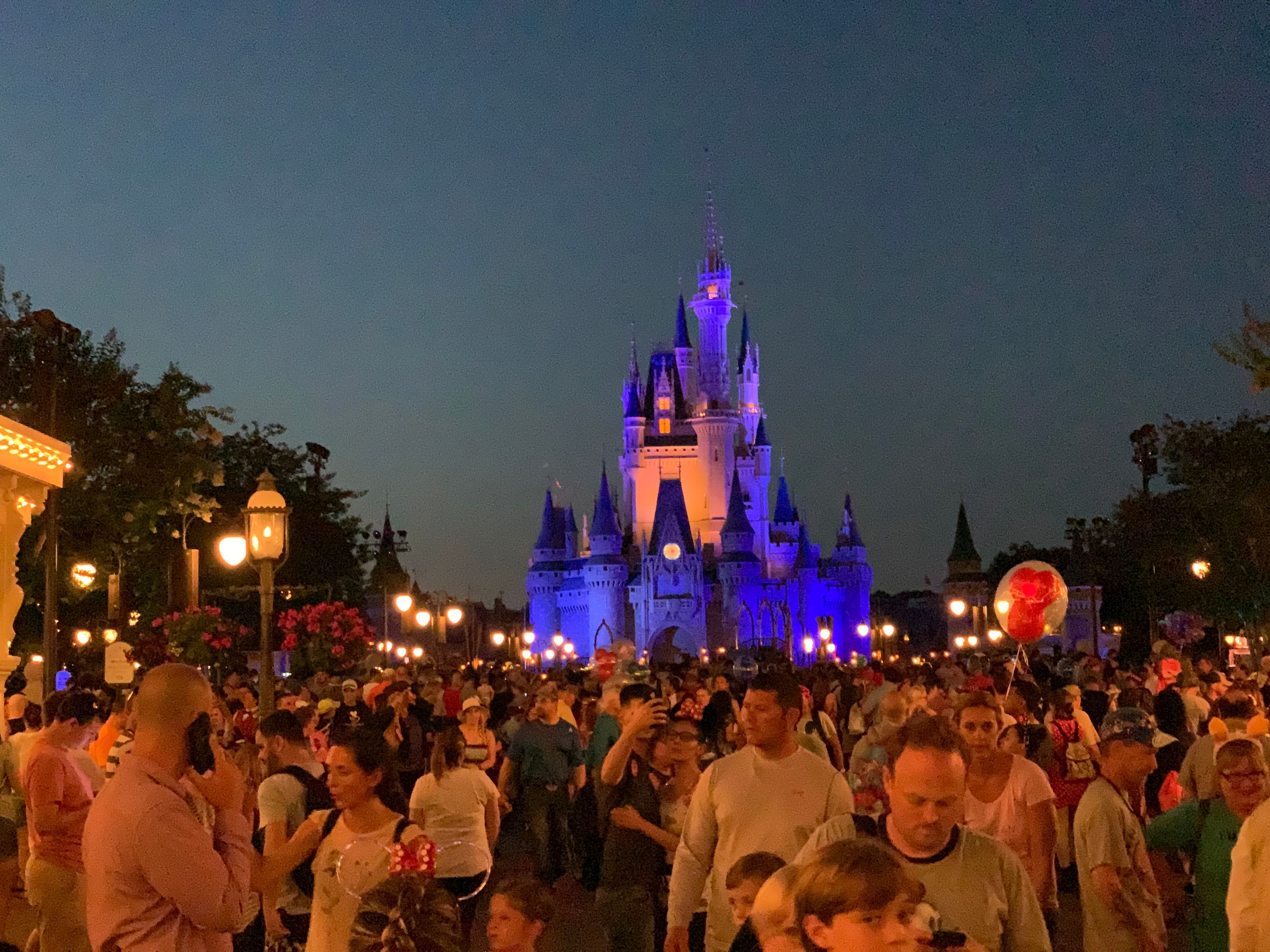 Cinderella’s Castle is lit up at night behind a crowd of people on Disney World’s Main Street USA.