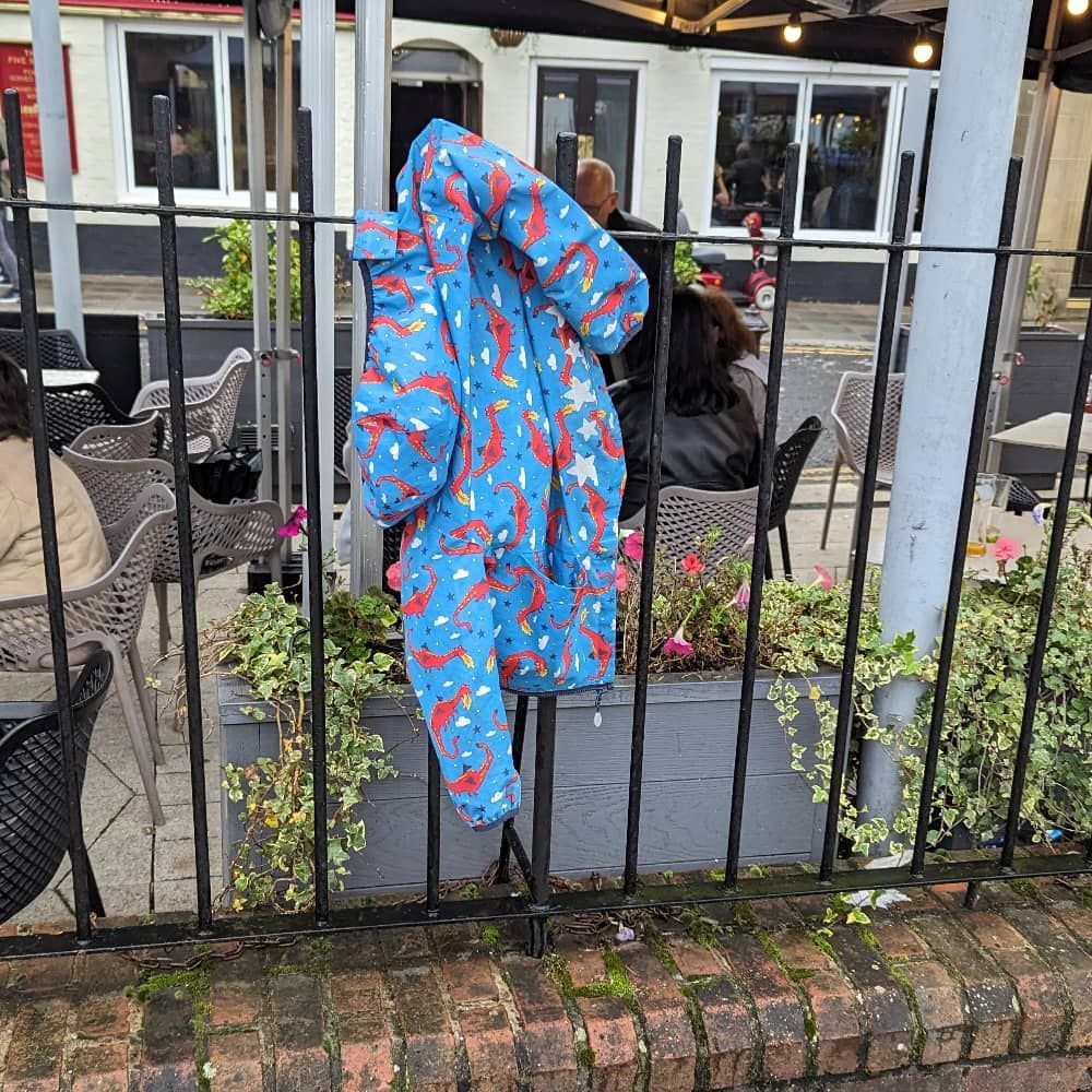 Kids’ jacket covered in fierce dragons and rain hangs forlornly on the iron railings penning in a Wetherspoons
