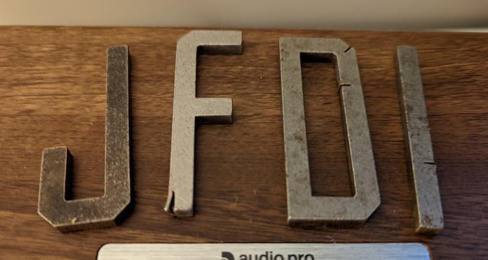 The letters J F D I in punch metal lying on a speaker
