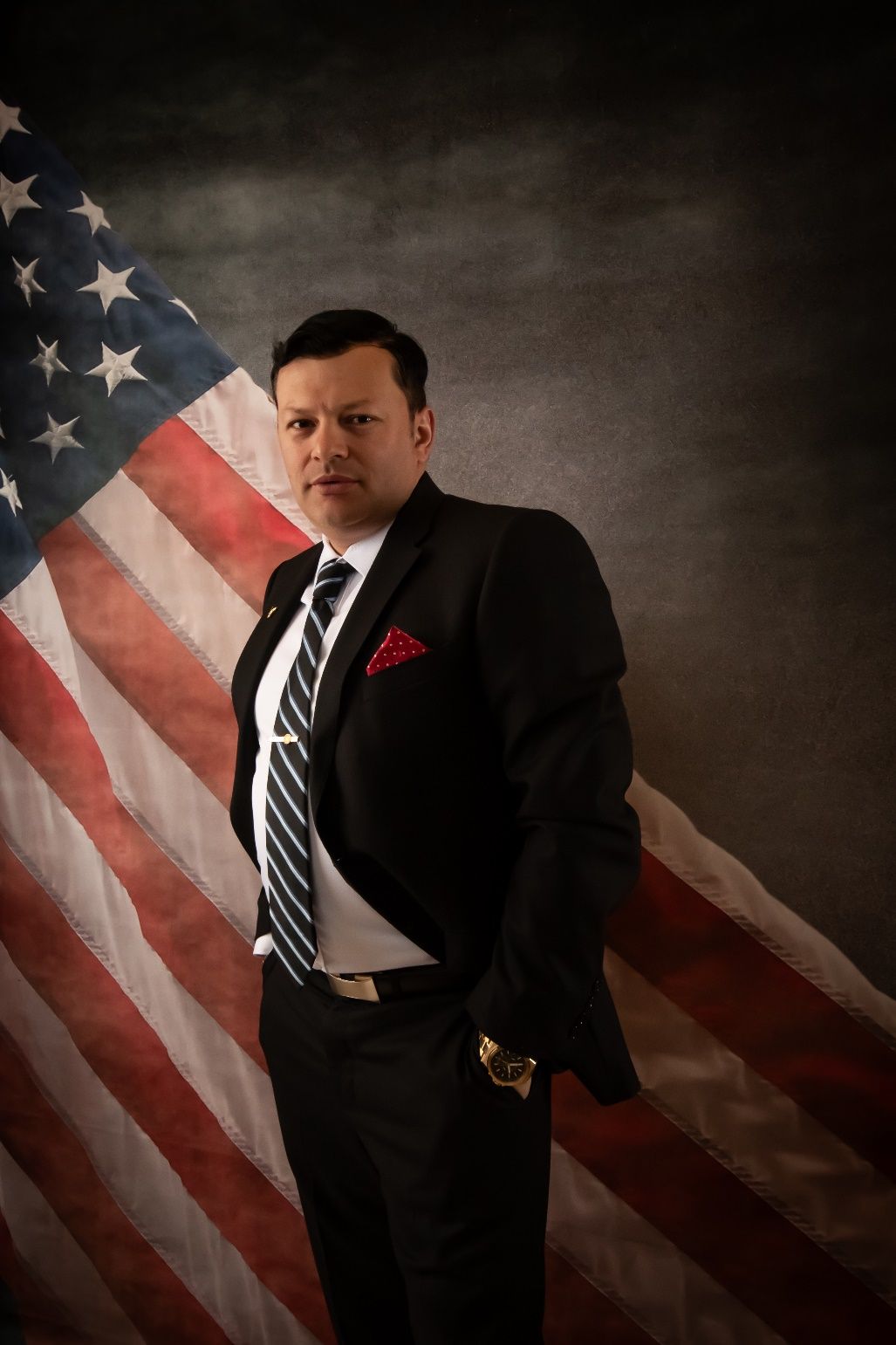 A person in a suit and tie standing in front of a flag Description automatically generated
