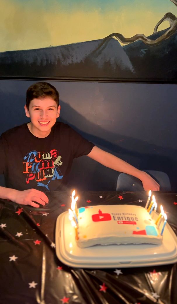 A child sitting at a table with a cake with candles Description automatically generated