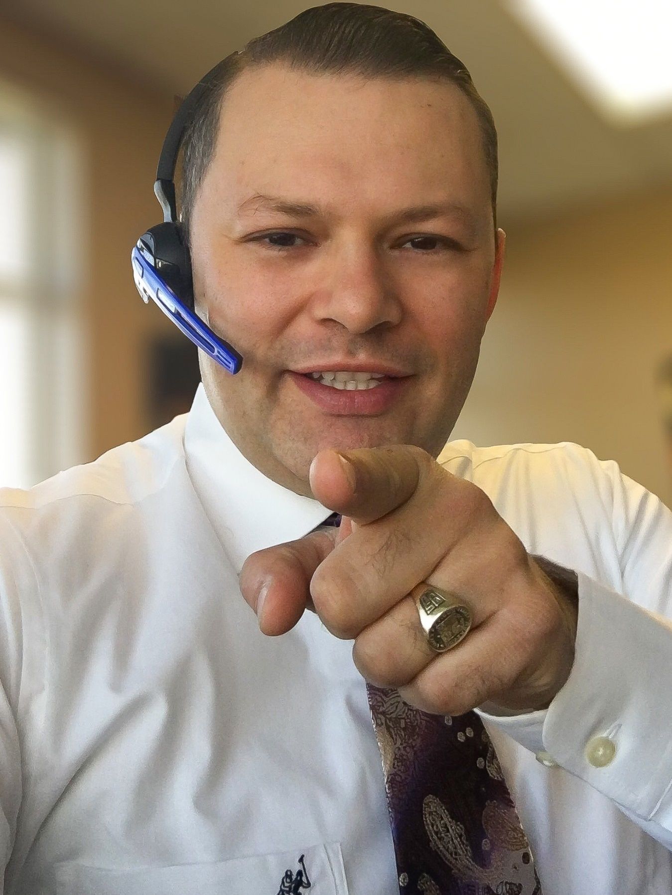A person wearing a headset pointing at the camera Description automatically generated