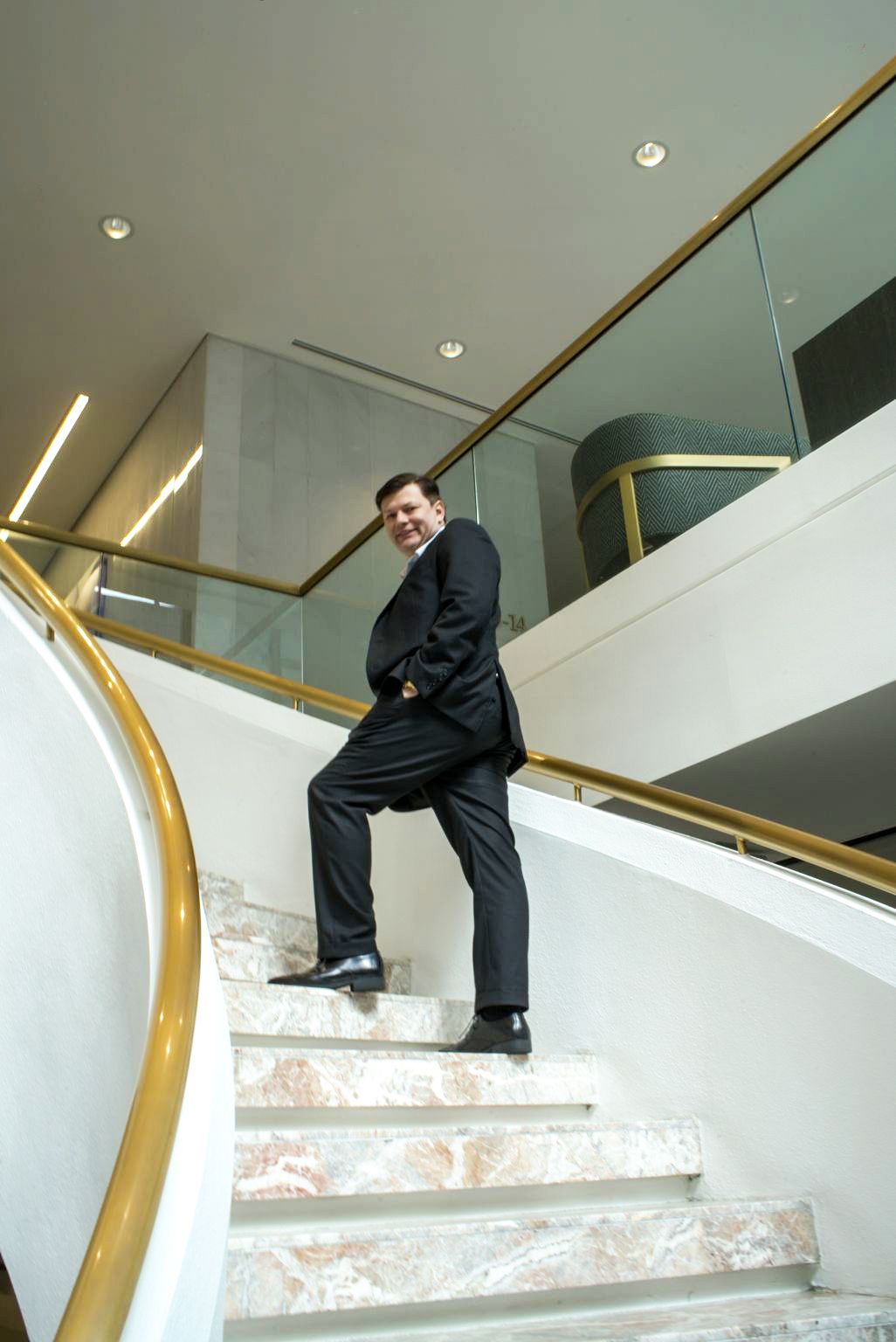 A person in a suit standing on a staircase Description automatically generated