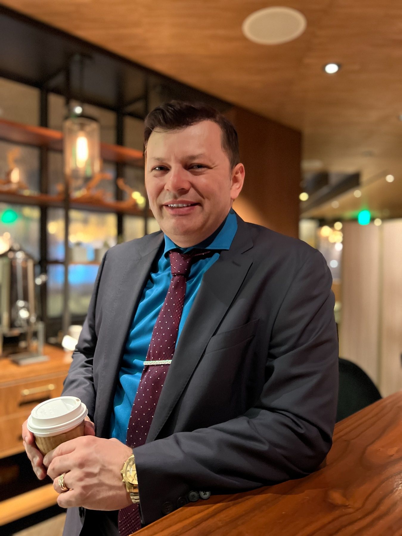 A person in a suit and tie holding a cup of coffee Description automatically generated