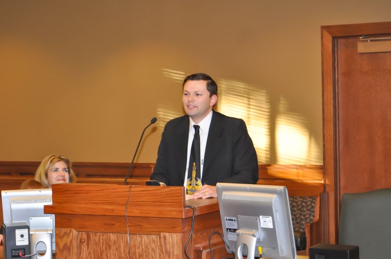 A person in a suit and tie standing at a podium Description automatically generated