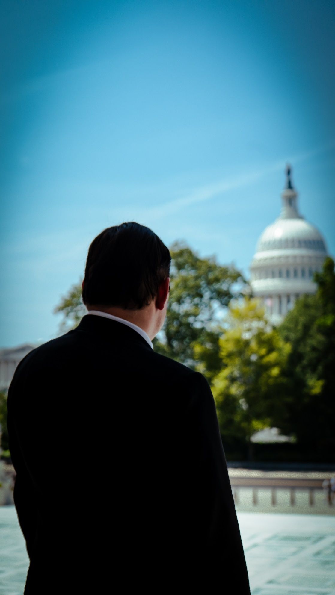 A person in a suit looking at the capitol building Description automatically generated