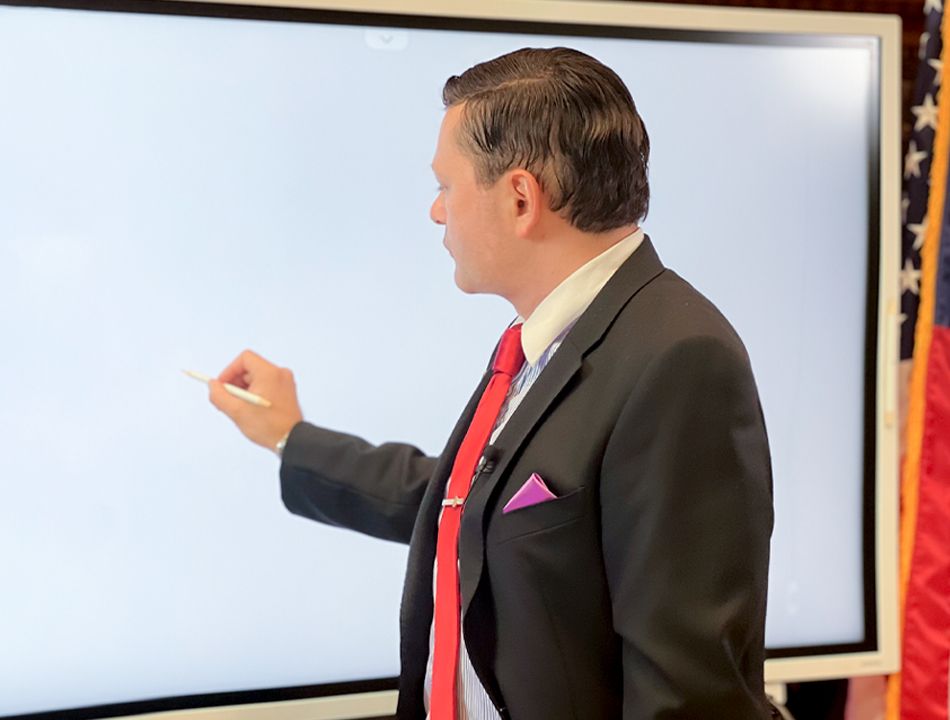 A person in a suit and tie writing on a white board Description automatically generated