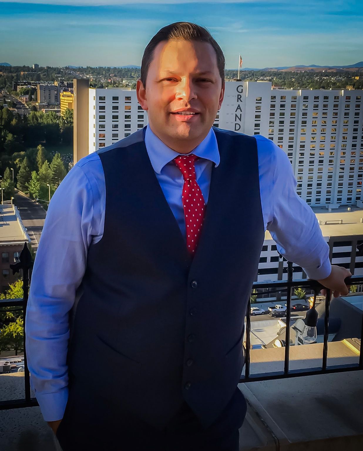 A person in a vest and tie standing on a balcony Description automatically generated