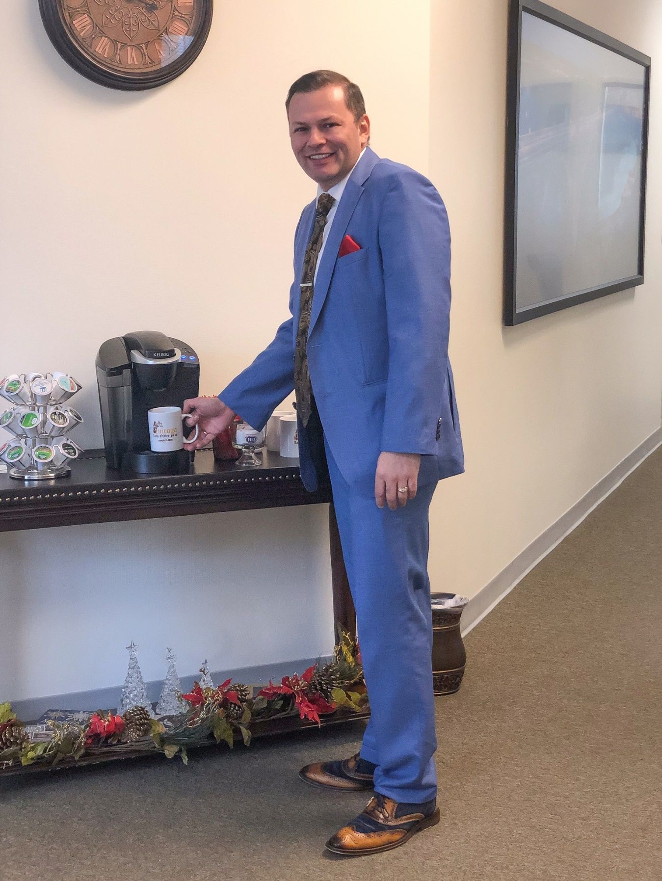 A person in a suit standing next to a coffee machine Description automatically generated