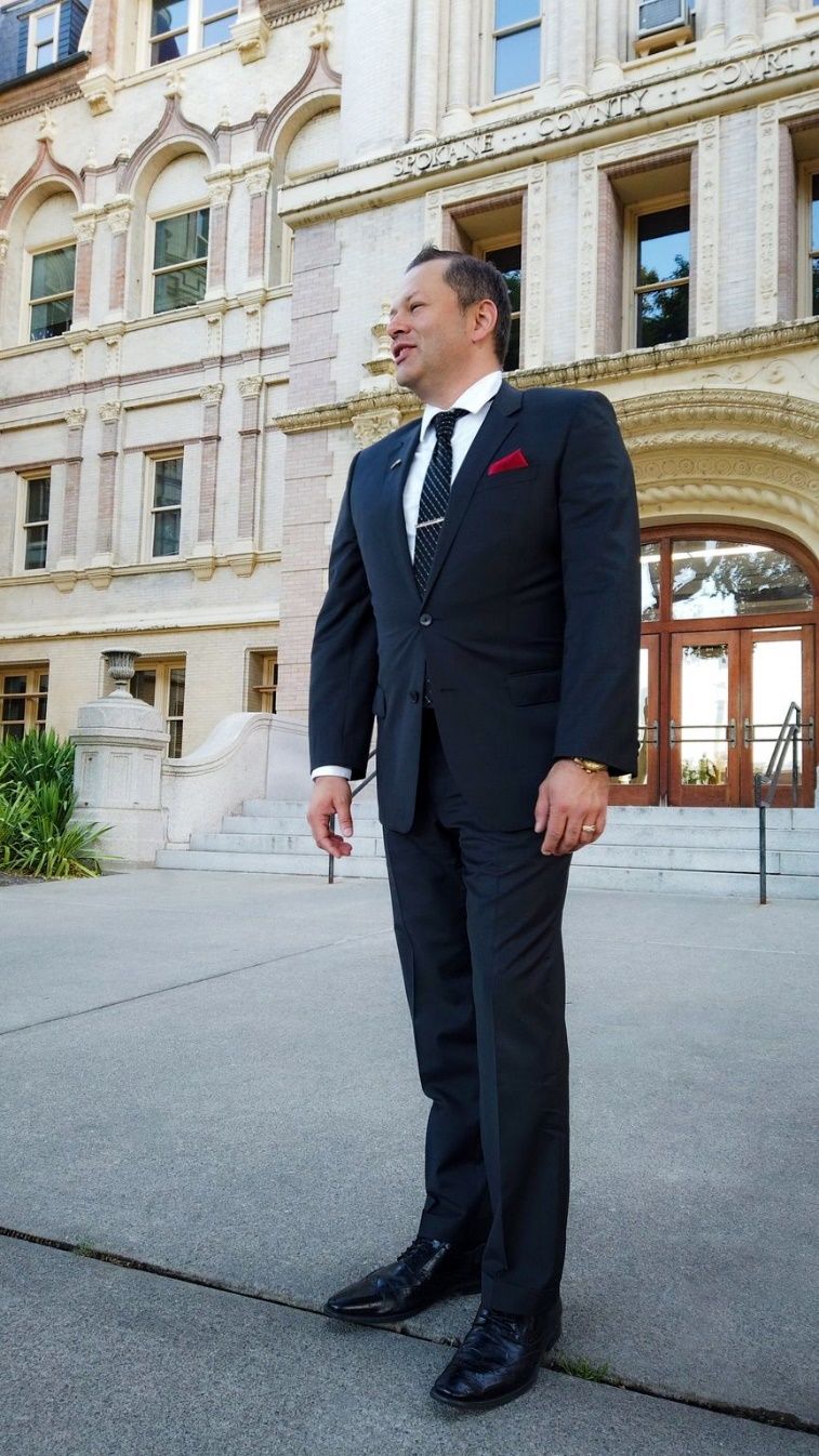 A person in a suit standing outside a building Description automatically generated