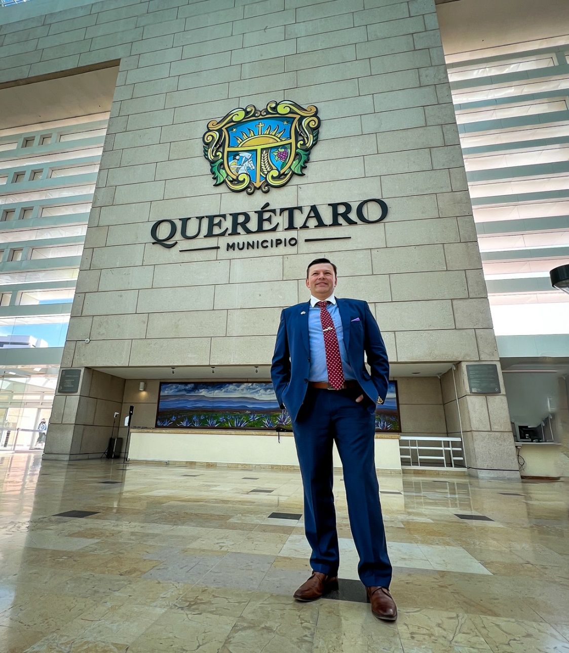 A person in a suit standing in front of a building Description automatically generated