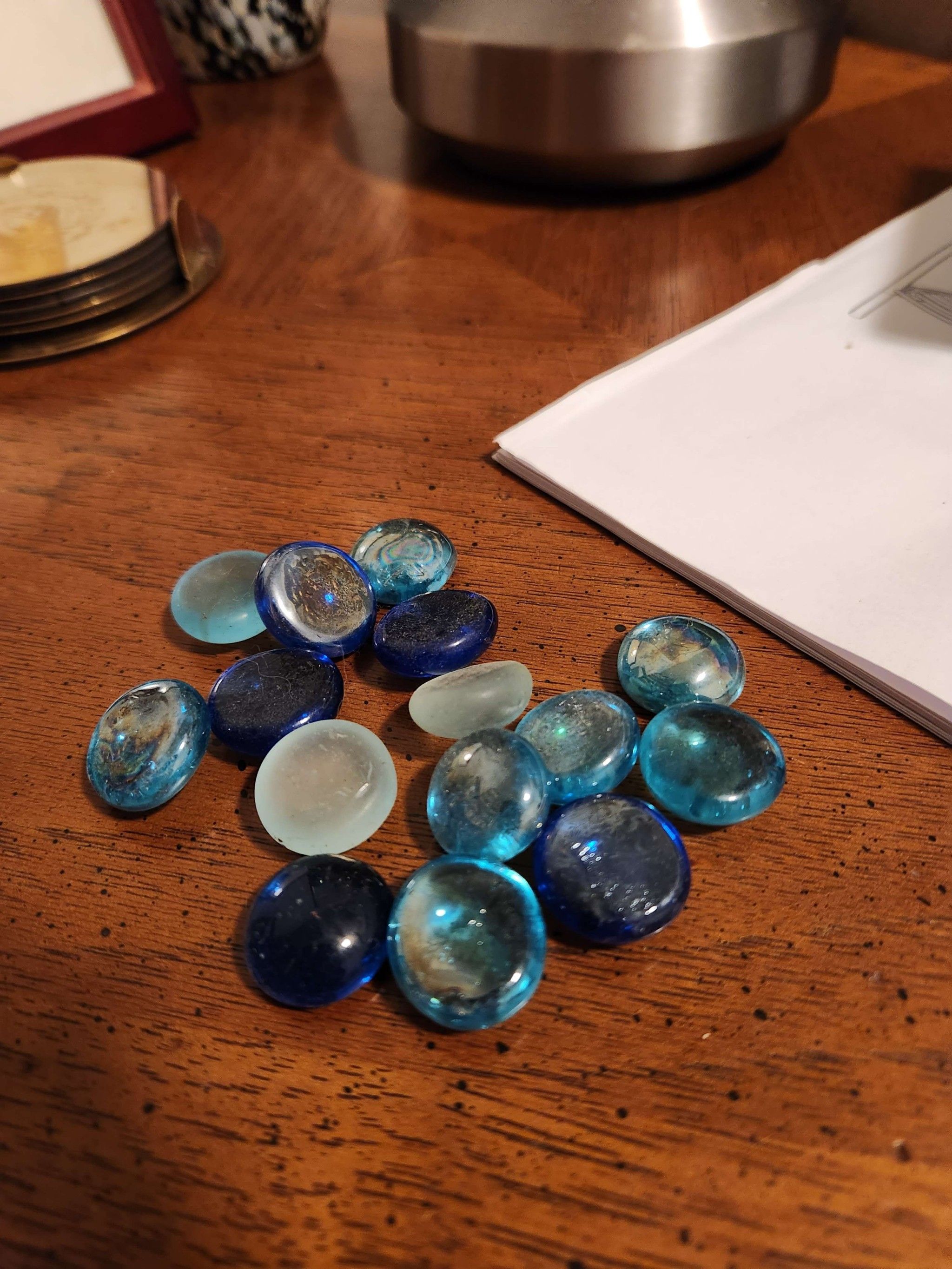 A small pile of blue flat glass beads on a wooden surface, with other things out-of-focus behind them.