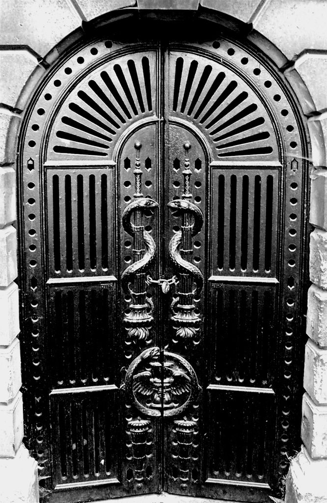 A closed pair of metal doors with embossed snake patterns, black-and-white photo.