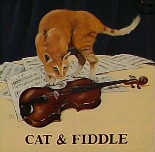 An orange cat stands on some scattered sheet music, sniffing a fiddle.
