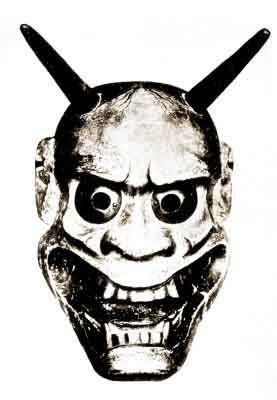 A greyscale photograph of a demon mask from a book of Japanese Nō plays. It has two straight black horns on its bald head, exaggerated facial features, and a wide smile that stretches the sides of its face.